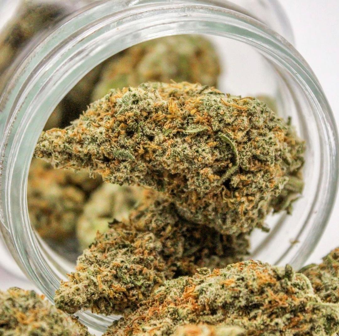 Close-up through a glass jar opening showing cannabis buds with orange hairs inside